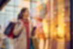 A woman smiling and looking at a shop window while carrying shopping bags